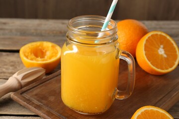Tasty orange juice in mason jar, fresh fruits and juicer on wooden table, closeup