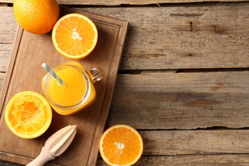 Tasty orange juice in mason jar, fresh fruits and juicer on wooden table, flat lay. Space for text