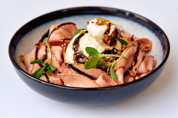 A Delicate Culinary Creation Featuring Slices of Savory Meat Accompanied by Creamy Cheese and Garnished with Nuts and Fresh Greenery in a Stylish Bowl