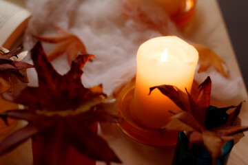 Burning candle creating cozy halloween atmosphere with autumn leaves and open book
