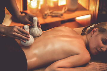 Hot herbal ball spa massage body treatment, masseur gently compresses herb bag on woman body....