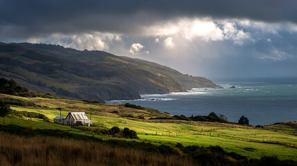 Dramatic coastal landscape with sunbeams piercing through stormy skies over a lone cabin