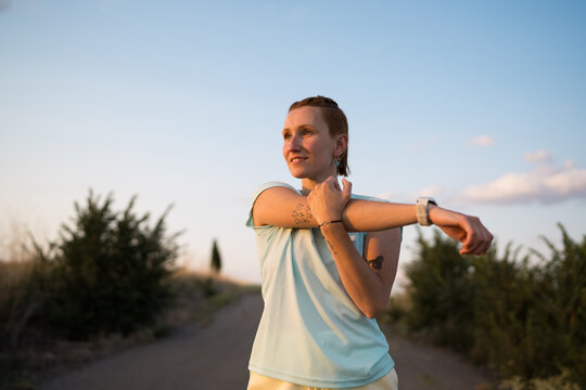 Young sporty woman stretching arms before running in countryside road