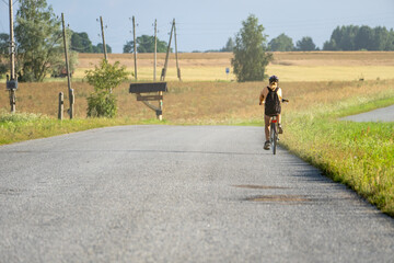 Child riding bicycle on quiet country road through rural landscape with fields and power lines on a warm summer day, symbol of freedom and simplicity