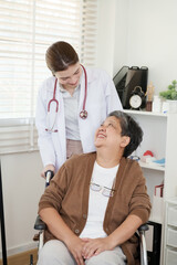 Asian elderly woman sitting in wheelchair looking up smiling at orthopedic doctor who gently leans...