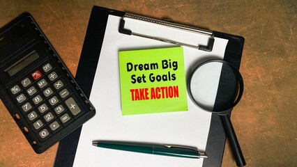 The words DREAM BIG SET GOALS TAKE ACTION are written on an isolated sticky note on the desk. A...