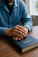 pensive caucasian man in blue shirt praying with hands on bible at wooden table in bright room reflecting faith and spirituality