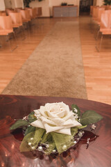 White rose with wedding rings resting on table in ceremony hall