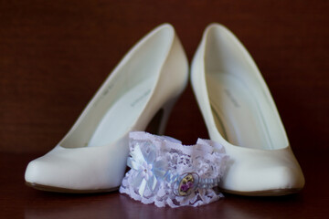 Elegant white wedding shoes and garter on wooden table