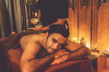 Masseur hands pouring aroma oil on man back. Masseuse prepare oil massage procedure for customer at...