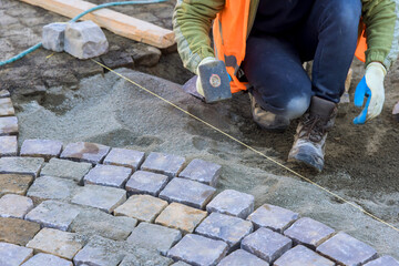 Craftsman arranging cobblestones with precision on construction site in ensuring quality work.