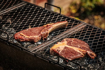 A thick-cut raw tomahawk steak rests on a hot metal grill, showcasing rich marbling and a long bone handle. Ideal for barbecue or steakhouse-style cooking.