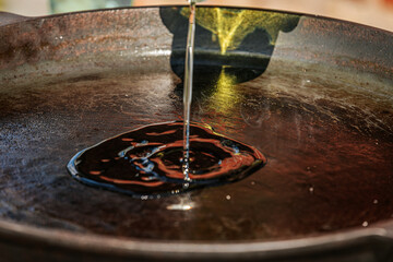 Obraz premium A stream of olive oil is being poured into a seasoned cast iron pan, creating a shiny pool in the center. The pan's dark surface contrasts with the golden oil.