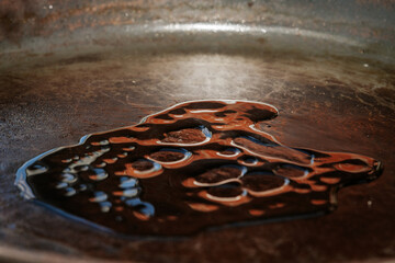 A stream of olive oil is being poured into a seasoned cast iron pan, creating a shiny pool in the...