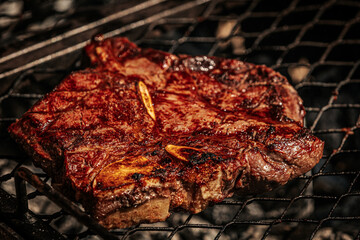 Close-up of juicy T-bone and tomahawk steaks sizzling on a charcoal grill, with one being turned...