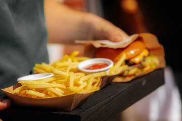 A close-up of a juicy cheeseburger with lettuce and sauce, served alongside golden French fries and a cup of ketchup on a rustic wooden tray.