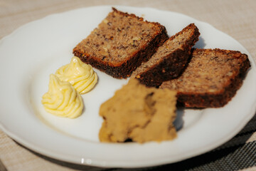 Plate with three slices of dark rye bread, a serving of liver pâté, and two decorative swirls of butter on a white dish atop a beige placemat.