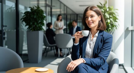 A woman takes a break in a modern office, holding a cup of coffee with people in the background. She exudes confidence and a calm, collected demeanor. The bright, open space enhances the scene
