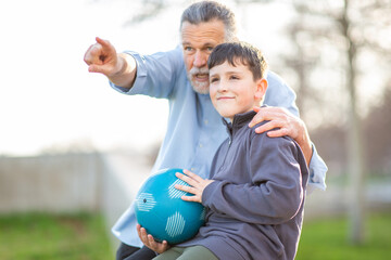 Grandfather pointing as boy sits with soccer ball
