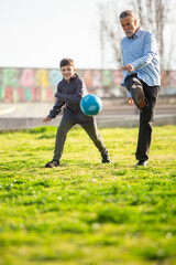 Fototapeta premium Smiling boy and grandfather kicking soccer ball together
