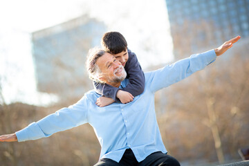 Grandfather with arms outstretched as grandson hugs from behind