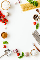 Frame of ingredients for cooking Italian pasta - uncooked spaghetti with tomatoes and basil leaves - on a white background, top view