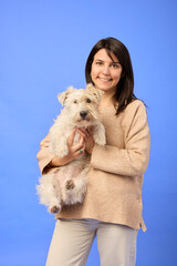 Caucasian woman smiling while holding Parson Russell Terrier on blue backdrop