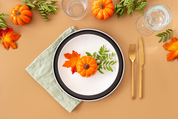 Festive Thanksgiving table setting with pumpkin in plate and cutlery - autumn leaves and tableware decorated on brown background, flat lay. Top view