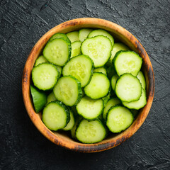 Sliced fresh green cucumber in a wooden bowl and a set of fresh cucumbers on the table. On a stone...