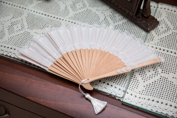 Elegant hand-crafted fan rests on a vintage lace tablecloth in a charming, sunlit room filled with...