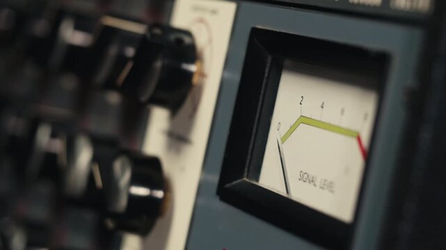 Analog dial indicator of audio signal level amplifier. Vintage arrow moves with sound level. Round classic volume indicator with yellow backlight, VU meters. Close-up of old measuring dB decibels
