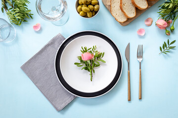 Festive table setting with empty plate, cutlery and napkin - flowers decorated, bread and olives for dinner, flat lay. Top view
