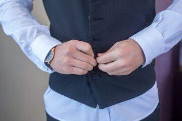 Stylish gentleman prepares for a special occasion, adjusting a vest with precision and elegance in...