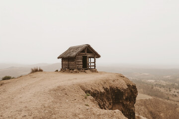 Rustic wooden cabin with thatched roof perched on a cliff edge overlooking a vast landscape