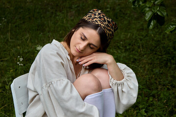 Serene young woman with leopard print bandana sitting on a white chair outdoors in nature, her head resting on her hand, lost in contemplation, in a peaceful scene in the garden