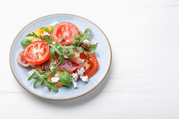 Tasty salad with arugula, cheese, tomatoes, nuts and prosciutto on white wooden table, above view. Space for text
