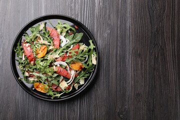 Tasty salad with arugula, cheese, grapefruit, vegetable and balsamic sauce on dark wooden table, top view. Space for text