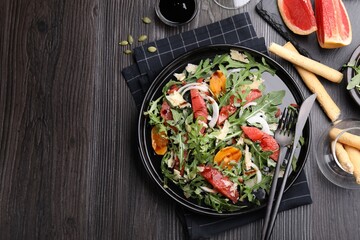 Tasty salad with arugula, cheese, grapefruit, vegetable and balsamic sauce served on dark wooden table, flat lay. Space for text