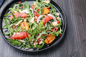 Tasty salad with arugula, cheese, grapefruit, vegetable and balsamic sauce on dark wooden table, above view
