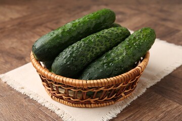 Fresh cucumbers in wicker basket on wooden table, closeup