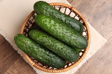 Fresh cucumbers in wicker basket on wooden table, top view