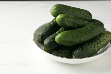 Fresh cucumbers in bowl on white table, closeup