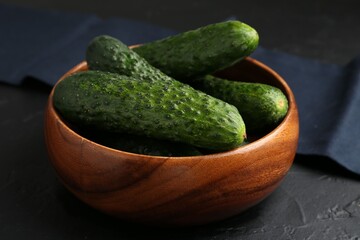 Fresh cucumbers in bowl on dark textured table, closeup