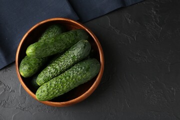 Fresh cucumbers in bowl on dark textured table, top view. Space for text