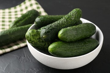 Fresh cucumbers in bowl on dark textured table, closeup