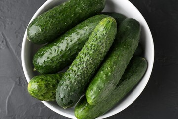 Fresh cucumbers in bowl on dark textured table, top view