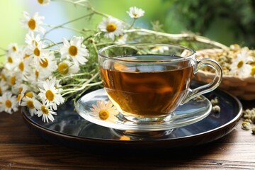 Tasty chamomile tea and flowers on wooden table, closeup
