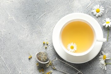 Tasty chamomile tea, infuser and flowers on light grey table, flat lay. Space for text