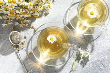 Tasty chamomile tea, infuser and flowers on light grey table, flat lay