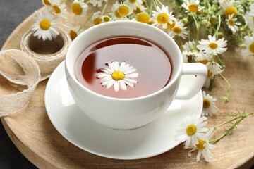 Tasty chamomile tea and flowers on black table, closeup